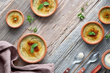 Creme brulee, or Crema Catalana, the Spanish variation of this traditional custard dessert, made in traditional cazuela dishes. Flat lay on rustic wooden table.