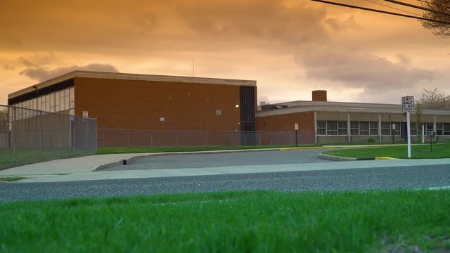 Sunset evening school exterior establishing 4k video shot. DX elementary high education building street view lock down. Beautiful orange sky and clouds overhead.