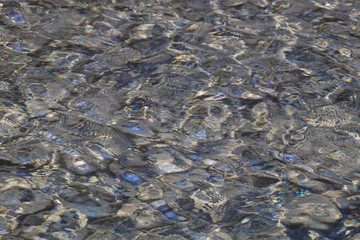 dispersion of sunlight on the surface of water in the mountain river. Through the water you can see the  contours of the stones at the bottom of the river. Abstract background