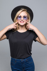 Portrait of funny young woman in black hat pointing index fingers on blowing cheeks isolated on...