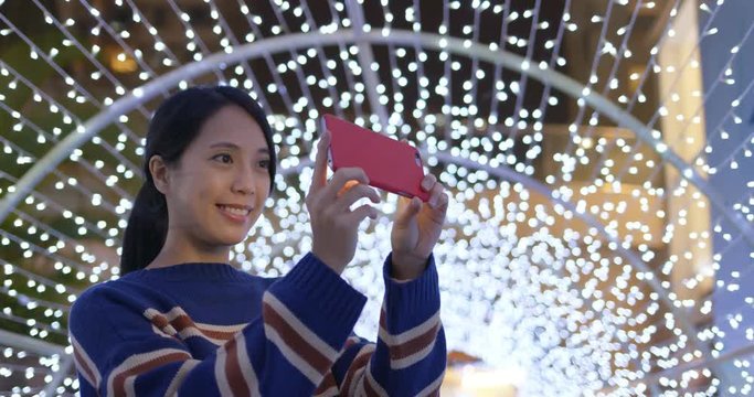 Woman take photo with cellphone under the background of light decoration at night