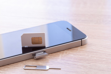 SIM card, the key to install the SIM card and smartphone is on a wooden table with purple tinted