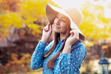 Beautiful young woman walking in autumn park. Gorgeous young woman in fall with big hat, smiling and enjoying nature