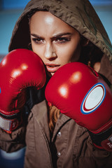 Portrait of female boxer in sport wear with fighting stance against spotlight. Sexy fitness blonde...