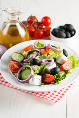 Fresh Greek salad made of cherry tomato, ruccola, arugula, feta, olives, cucumbers, onion and spices. Caesar salad in a white bowl on wooden background. Healthy organic diet food concept.