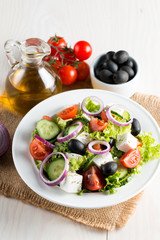 Fresh Greek salad made of cherry tomato, ruccola, arugula, feta, olives, cucumbers, onion and spices. Caesar salad in a white bowl on wooden background. Healthy organic diet food concept.