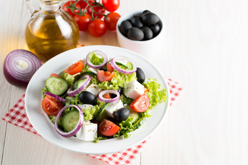 Fresh Greek salad made of cherry tomato, ruccola, arugula, feta, olives, cucumbers, onion and spices. Caesar salad in a white bowl on wooden background. Healthy organic diet food concept.