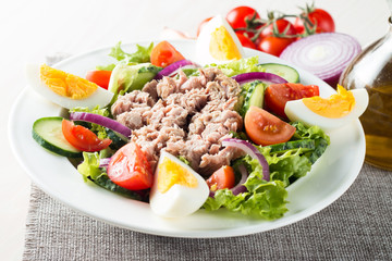 Fresh fish tuna salad made of tomato, ruccola, tuna, eggs, arugula, crackers and spices. Caesar salad in a white bowl on wooden background