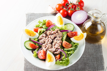 Fresh fish tuna salad made of tomato, ruccola, tuna, eggs, arugula, crackers and spices. Caesar salad in a white bowl on wooden background