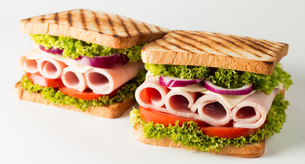 Close-up photo of a club sandwich. Sandwich with meat, prosciutto, salami, salad, vegetables, lettuce, tomato, onion and mustard on a fresh sliced rye bread on wooden background. Olives background.
