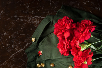 against the background of the monument, a bouquet of red carnations, military uniform and field cap