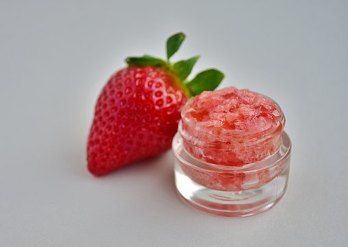 Diy strawberry lip scrub in small glass jar, homemade natural cosmetic, gray background.