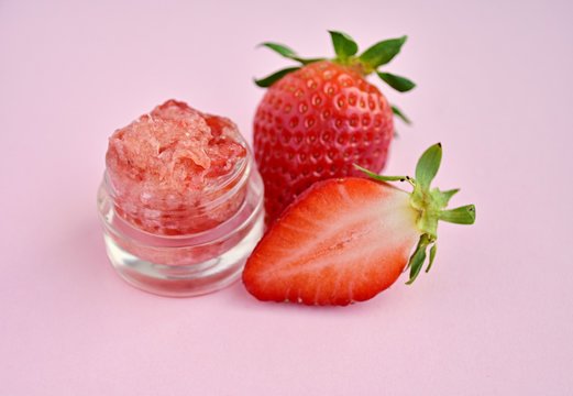 Strawberry, coconut oil and brown sugar lip scrub in small glass jar, fresh berries, pink background.