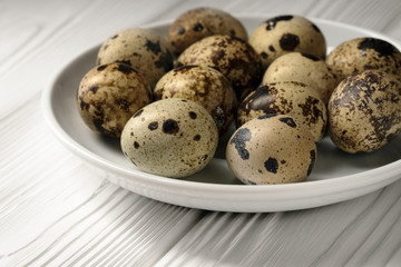 Side view of a white plate with quail eggs on a white wooden table