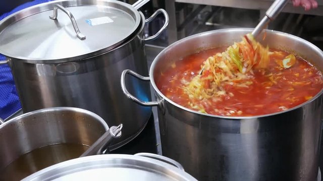A cook in a restaurant mixes borsch in a large pan in close-up, traditional Russian-Ukrainian cuisine