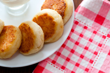 Cheese pancakes with sour cream on a white plate on a pink napkin with a fork, top view. Can be used for menu design.