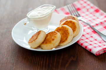 Cheese pancakes with sour cream on a white plate with a pink napkin and fork. Can be used for menu...