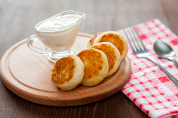 Cheese pancakes with sour cream on a wooden board with a fork. Can be used for menu design, culinary sites.