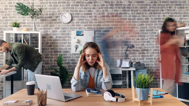 Zoom in time-lapse of exhausted female employee suffering from sick headache sitting in office at desk touching head. Tired people and workplace concept.