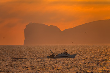 Fototapeta na wymiar A fishing boats crosses the waters in front of Capo Caccia near Alghero, Sardinia, Italy