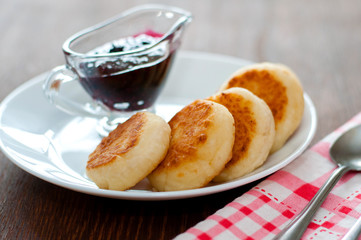 Cheese pancakes with jam, on a white plate, with a teaspoon, a fork and a kitchen towel