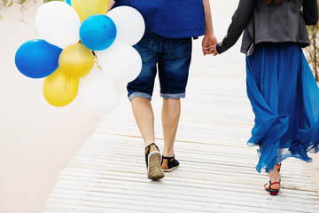 Fototapeta na wymiar Loving couple walking on a pier in hands with balloons. 