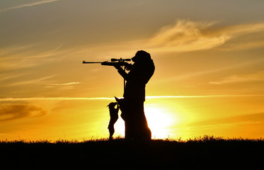Silhouette of a girl with a rifle at sunset and two dogs, a breed of Belgian Shepherd dog Malinois and a miniature pinscher