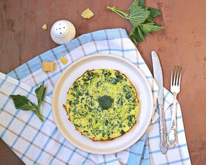 Breakfast, omelet with nettles on a white clay plate. Healthy food. Food from wild herbs. Top view, copy space.