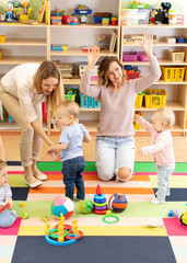 Babies toddlers playing with colorful educational toys together with mothers in nursery room