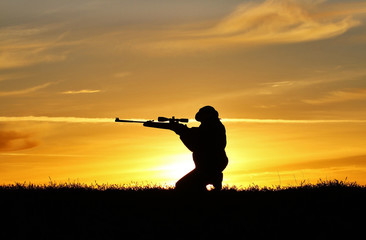 Fototapeta na wymiar Silhouette of a man with a rifle on the background of a beautiful sunset, the boy shoots a gun