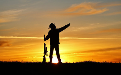 Silhouette of a man with a rifle on the background of a beautiful sunset, the boy shoots a gun