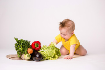 Fototapeta premium baby girl smiling in yellow bodysuit on white background with vegetables, baby food concept