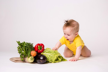 baby girl smiling in yellow bodysuit on white background with vegetables, baby food concept