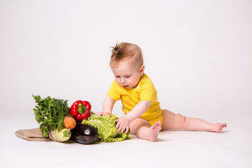 baby girl smiling in yellow bodysuit on white background with vegetables, baby food concept