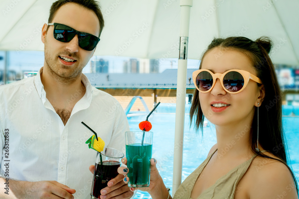 Wall mural young beautiful couple eating fast food by the pool, loving guy and girl eating burger and smiling a