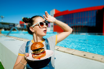 A girl with a Burger by the pool, a model in sunglasses holding a Burger. The concept of juicy burgers.