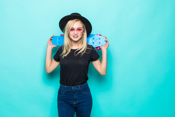 Young blonde girl in black fluffy hat holding a skateboard and looking at the camera isolated on green background