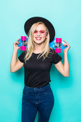 Portrait of blonde woman in sunglasses posing with skateboard while standing and looking at camera isolated over green background