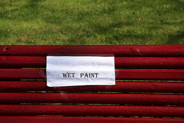Inscription 'Wet paint' on a sheet of white paper on red wooden bench, park improvement