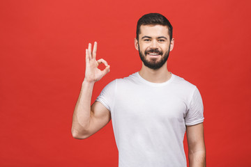Fototapeta premium Portrait of a cheerful young man showing okay gesture isolated on the red background.