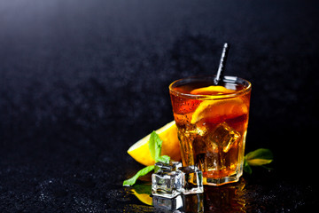 Traditional iced tea with lemon, mint leaves and ice cubes in glass on wet black background.