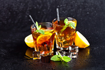 Two glasses with cold traditional iced tea with lemon, mint leaves and ice cubes.
