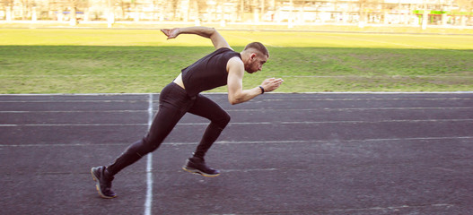 one caucasian male is doing a sprint start. running on the stadium on a rubber track. Track and field runner in sport uniform. energetic physical activities. outdoor exercise, healthy lifestyle