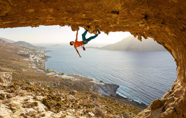 Male rock climber on challenging route going along ceiling in cave
