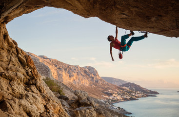 Caucasian man climbing challenging route going along ceiling in cave at sunset