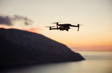 Fototapeta na wymiar Drone quadcopter with digital camera flying over coast at sunset