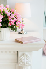 pink roses in a jug on a bookshelf