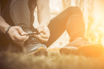 A young man in black clothes is tying the laces on the sneakers close up. fitness athlete sitting on the sports field on the grass. warm up body preparation for the training