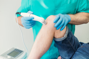 Close up Young man receiving laser or magnet therapy massage on a knee to less pain. A chiropractor...