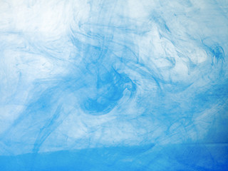 Blue acrylic ink dissolving into water, close up view. Blurred background. Acrylic light clouds moving in liquid, abstract background. Blue paint mixing with water, abstract pattern